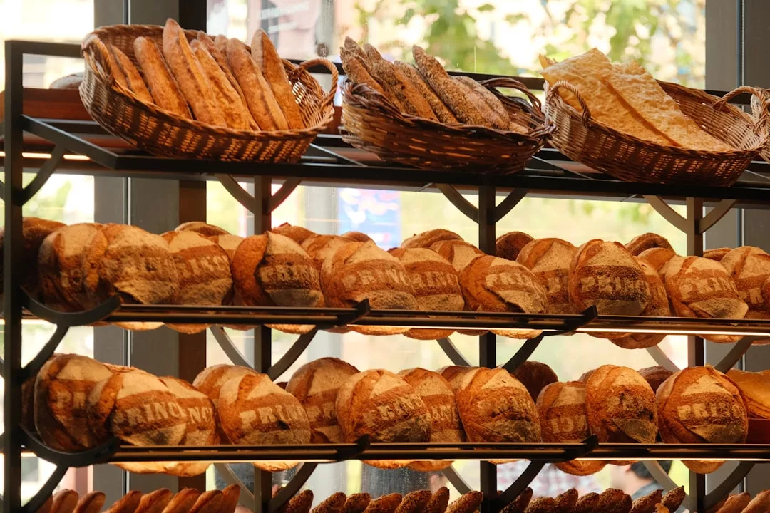 Shelves of assorted breads and baguettes in baskets at an artisan bakery, with sunlight streaming through a window in Esporles.