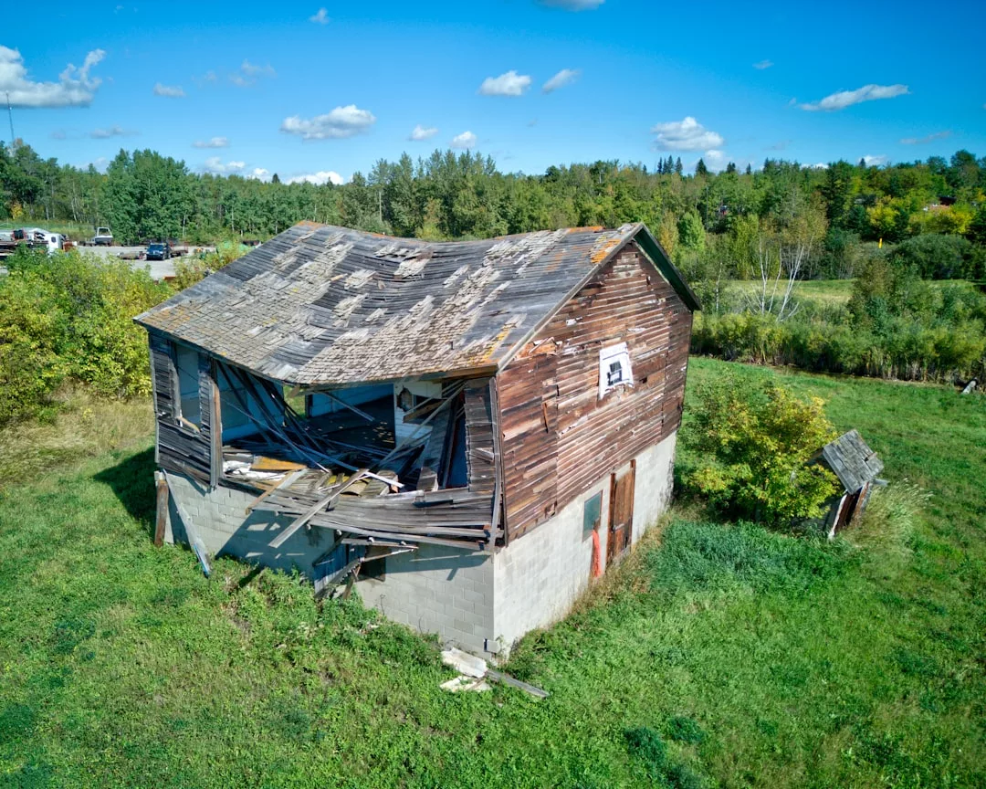 A dilapidated wooden barn with a sagging roof stands in a grassy field under a blue Palma sky, reminiscent of old repossessed properties left behind after auction pitfalls.