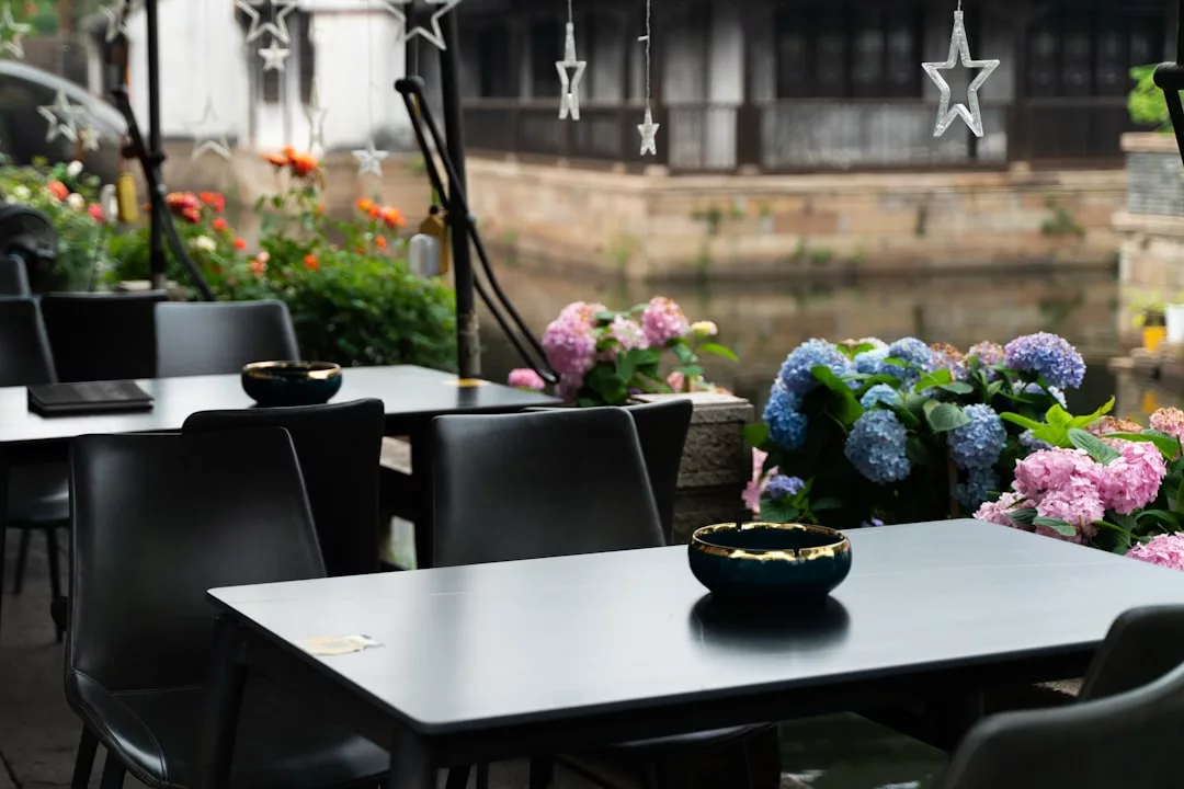Outdoor cafe tables by a canal in Porto Cristo, decorated with flowers, hanging star lights, black chairs, perfect for candlelit dinners.