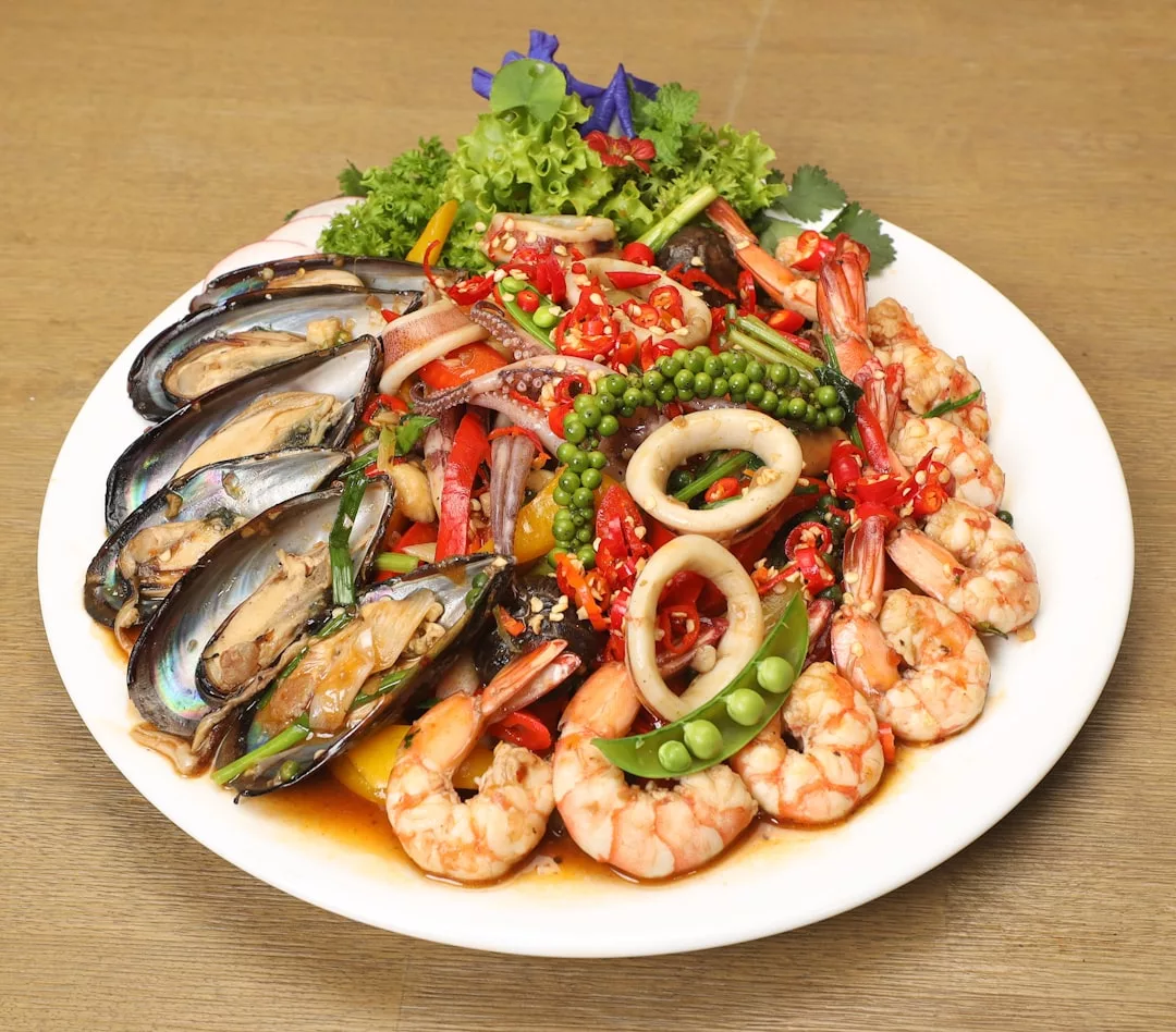A plate of mixed seafood with shrimp, mussels, squid, chili, and vegetables in a savory sauce—perfect for enjoying at clifftop seafood grills overlooking Port de Pollença.