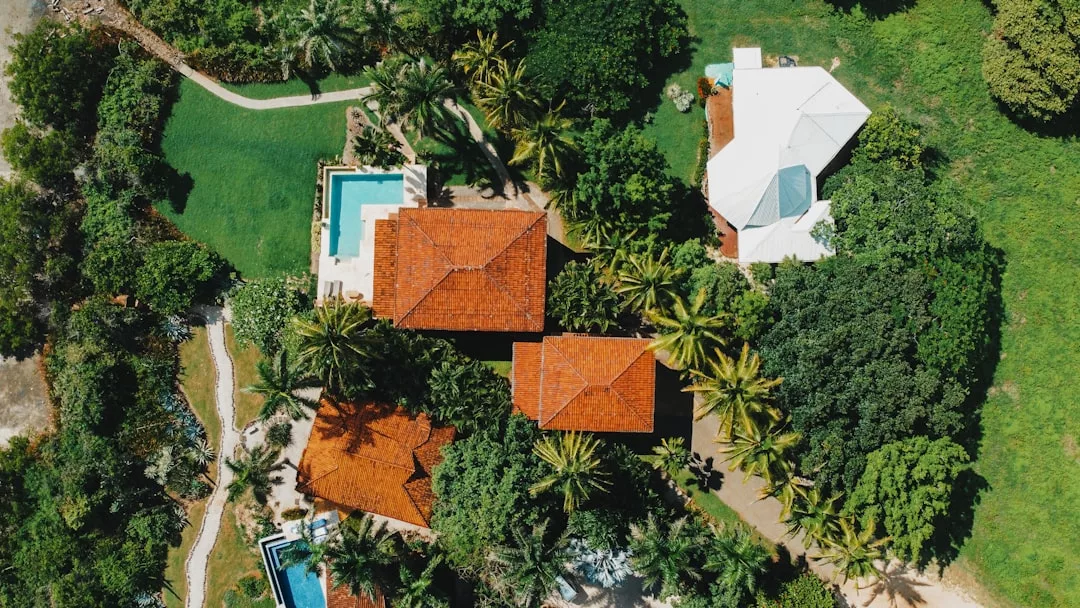 Aerial view of red-roofed houses, a white house, pools, and lush green trees and lawns in Cala Ratjada’s desirable coastal estate.