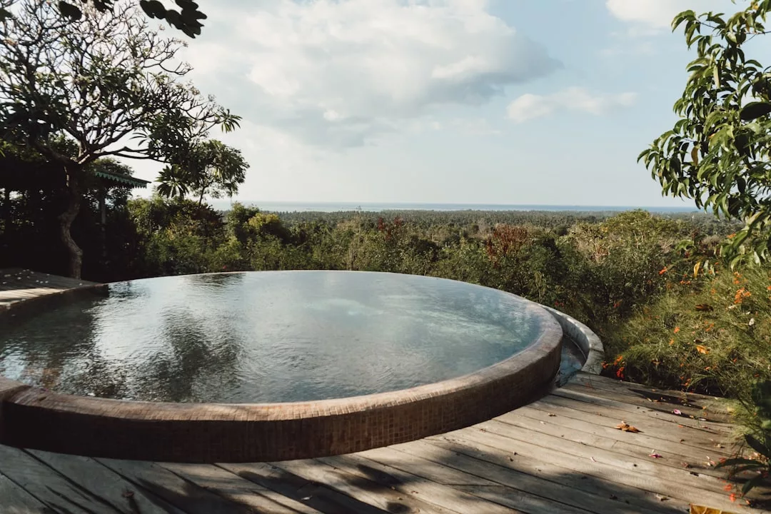 A round infinity pool in Llucmajor overlooks lush greenery and a distant ocean under a partly cloudy sky, offering the ultimate in luxury pools often found on exclusive fincas.