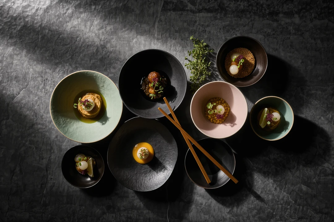 Assorted ceramic bowls in green, black, and pink on a dark surface, viewed from above—perfect for serving fusion-cuisine at stylish pop-ups in Pollença.