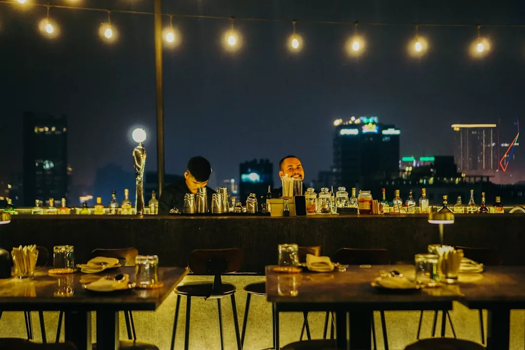Rooftop bar at night with two bartenders, string lights, and city buildings in the background—one of Palma’s chic rooftop restaurants near Passeig del Born.