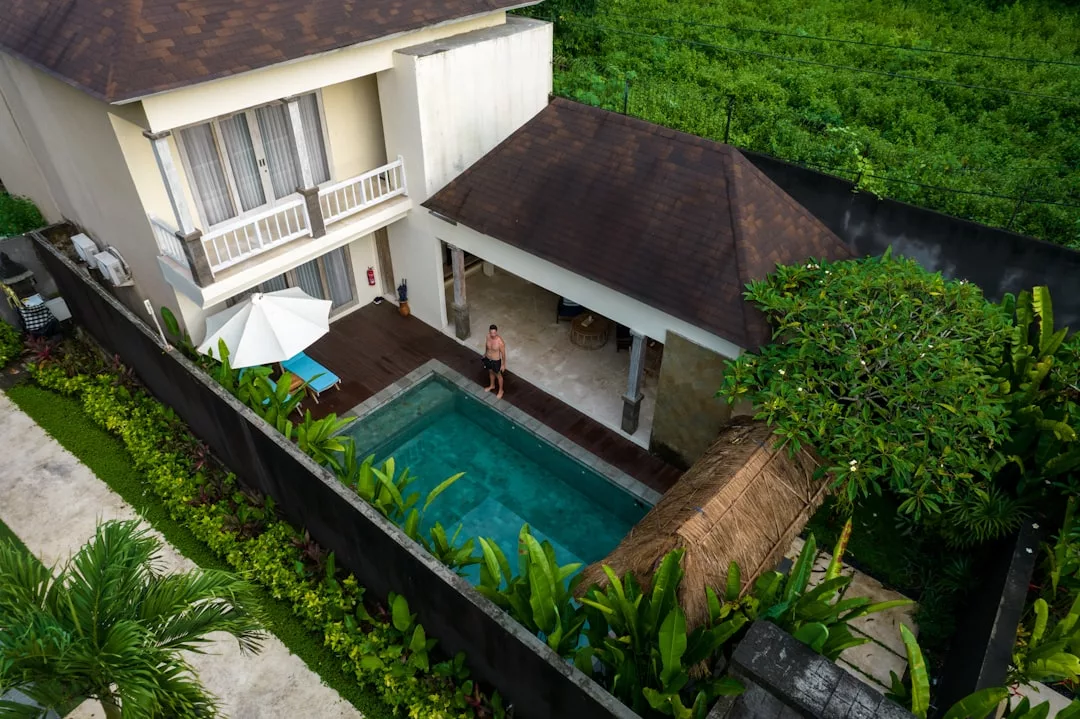 A person stands by a private pool beside a modern villa surrounded by lush greenery and tropical plants, showcasing the elegance of fincas often admired on architecture tours Andratx.