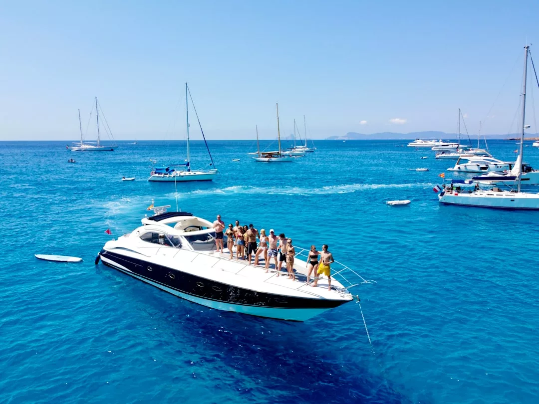 A group of people stand on a yacht in clear blue water near Port d’Andratx in southwest Mallorca, surrounded by several other boats on a sunny day—an idyllic scene perfect for yacht charters.