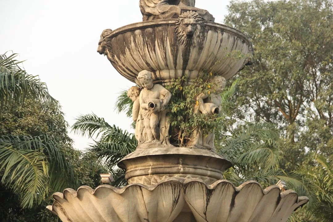 Ornate stone fountain with cherub statues and lion heads, surrounded by lush green trees and plants—a striking feature often found in luxury garden design at exclusive Andratx fincas.