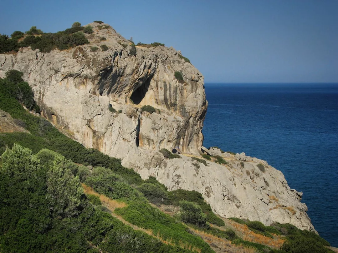 Large rocky cliff with sparse vegetation overlooks a calm blue sea under a clear sky, creating one of those Pinterest-perfect landscapes ideal for luxury photo backdrops near Banyalbufar.