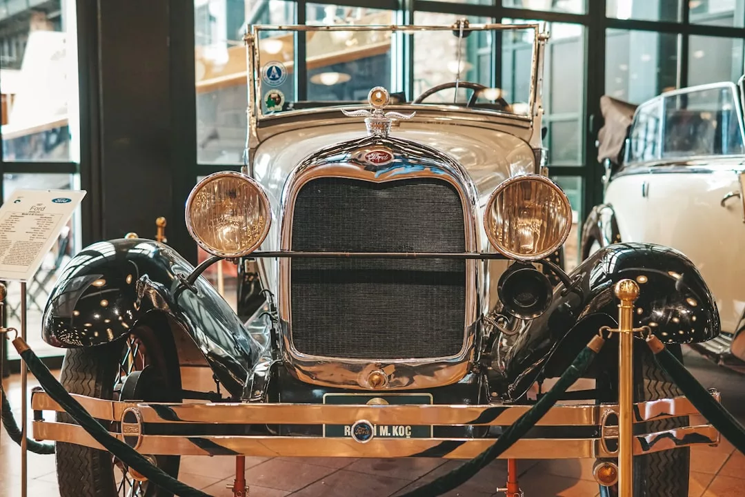Front view of a vintage silver car displayed indoors behind rope barriers, evoking the elegance of Boutique Journeys and Luxury Travel, with other classic cars nearby.