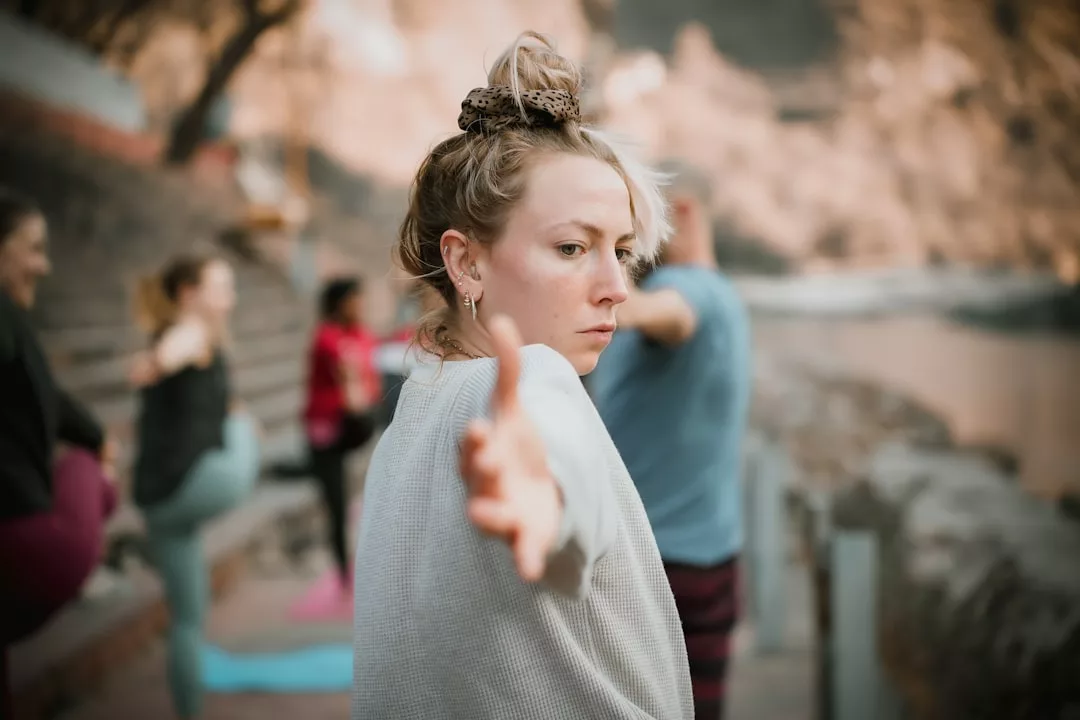 Woman practicing yoga outdoors in Esporles, extending her arm forward, with others blurred in the background—an inspiring scene that captures the essence of premium wellness and transformative wellness workshops.