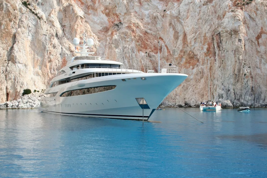 A large white yacht anchored near rocky cliffs in clear blue water near Cala Figuera, with smaller boats nearby—perfect for exclusive day trips or private island hopping adventures.