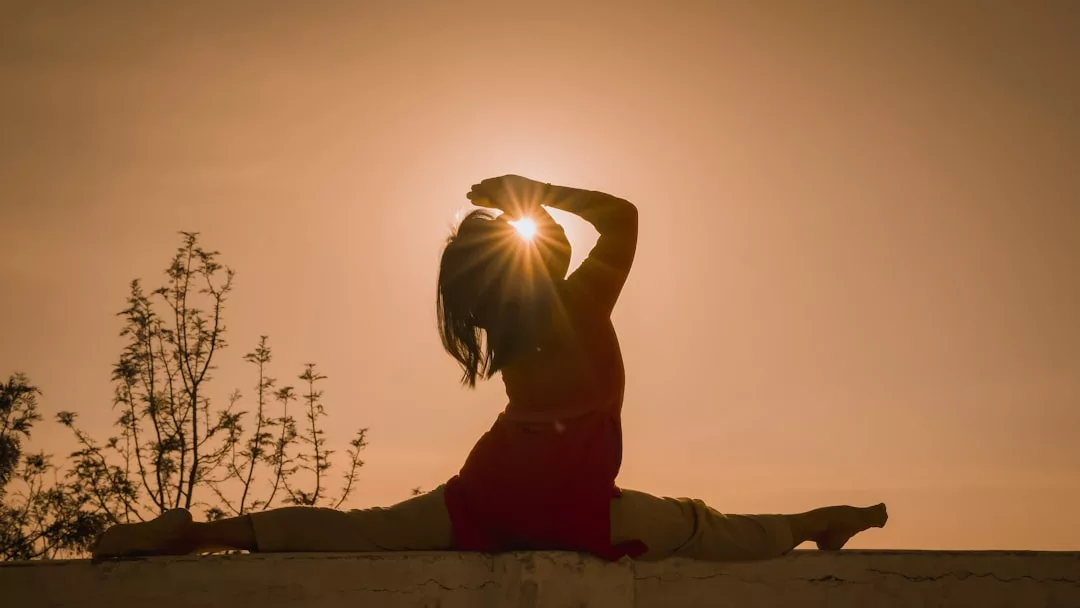 Person doing a split yoga pose outdoors at sunset in Deià, with the sun shining behind their head—a serene moment from one of our Mountain Yoga Retreats.