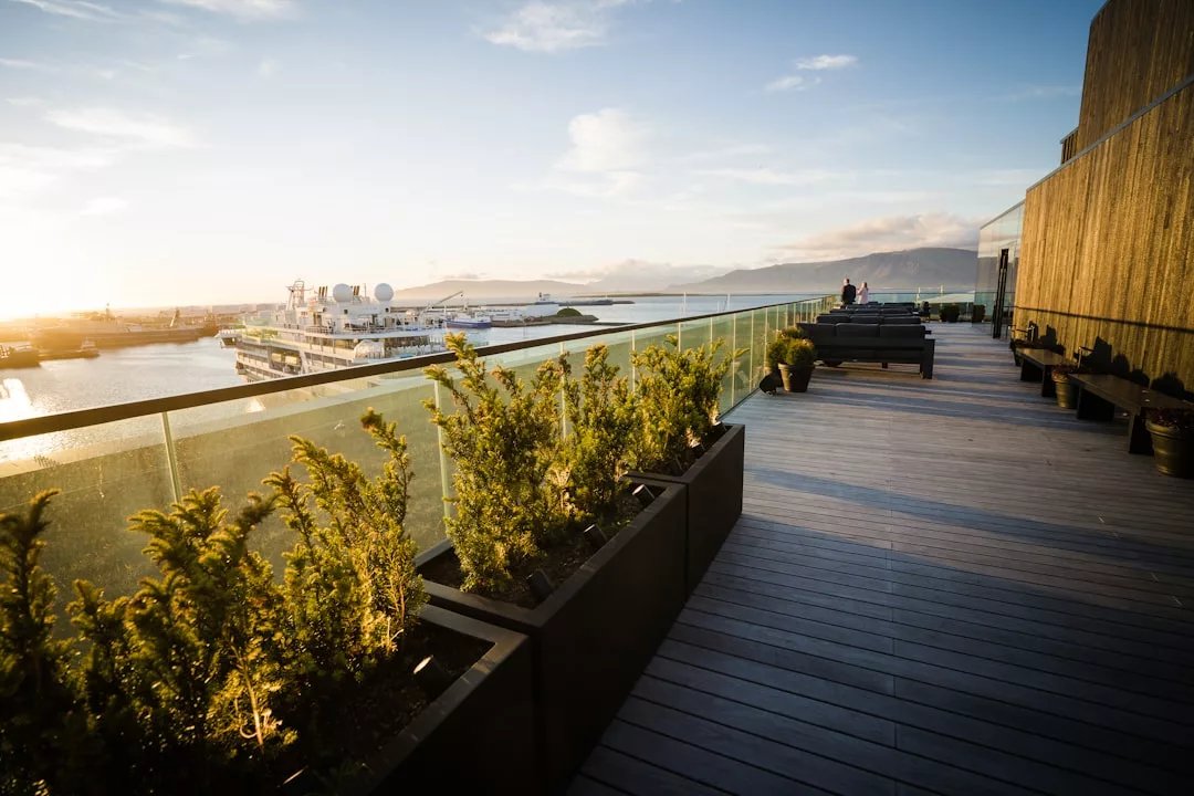 Rooftop terrace with plants, glass railing, and a view of Palma Carmen district's harbor at sunset—perfect for rooftop pizza and a glass of prosecco.