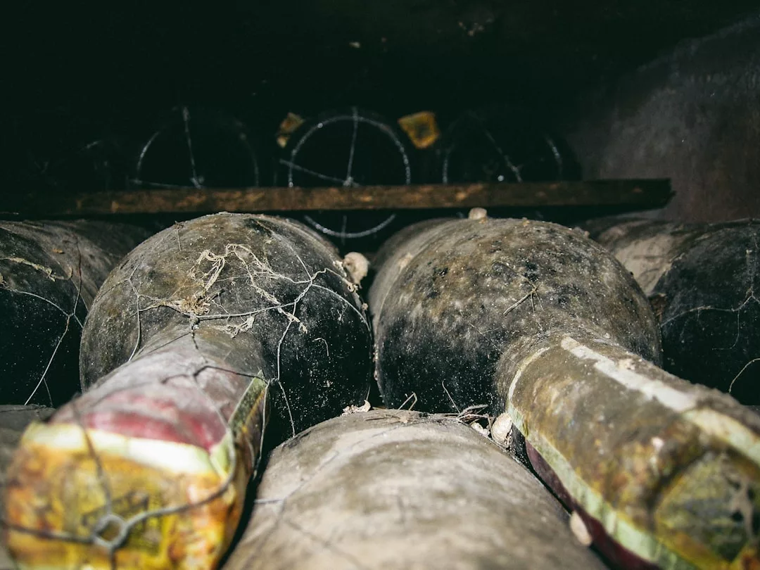 Dusty wine bottles covered in cobwebs are stacked in a dimly lit cellar, evoking the rich heritage of Binissalem and the vineyard restaurants known for their exquisite seasonal tasting menus.