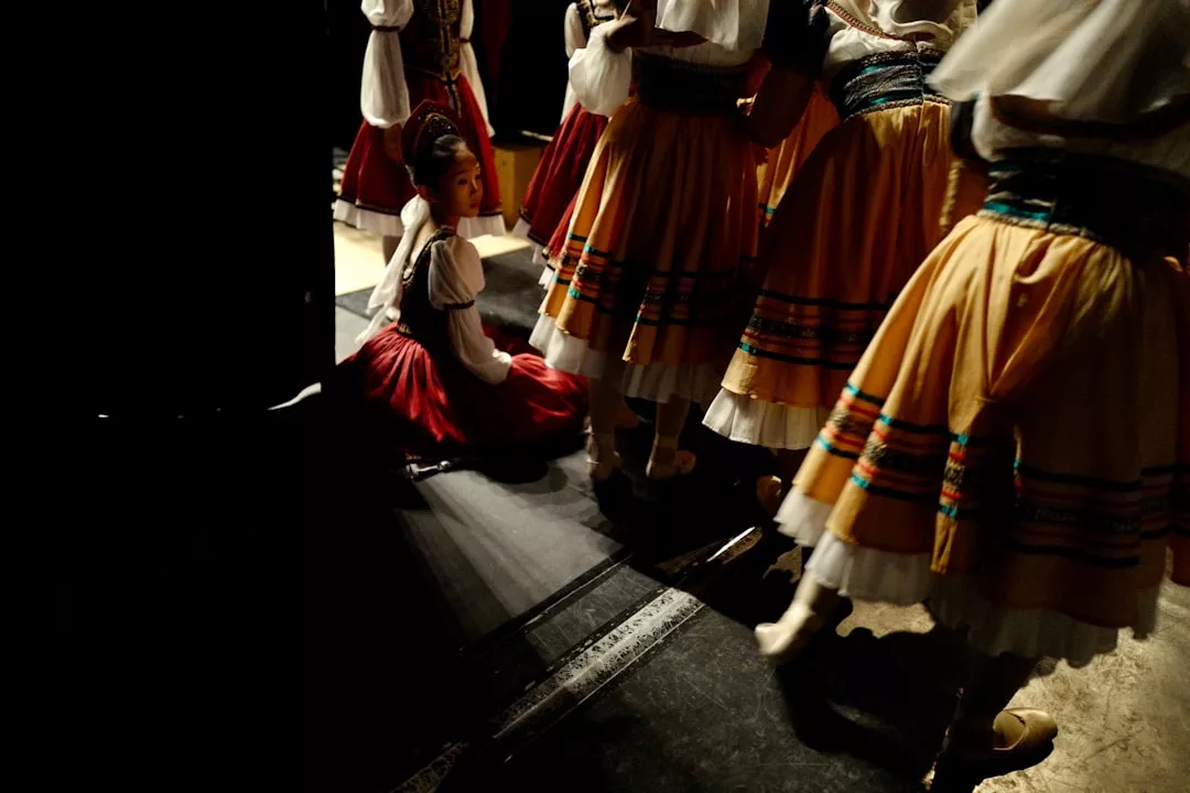 A girl in a red and white flamenco costume sits backstage as dancers in yellow skirts move past her, capturing the vibrant spirit found in tapas bars and restaurants in Palma.