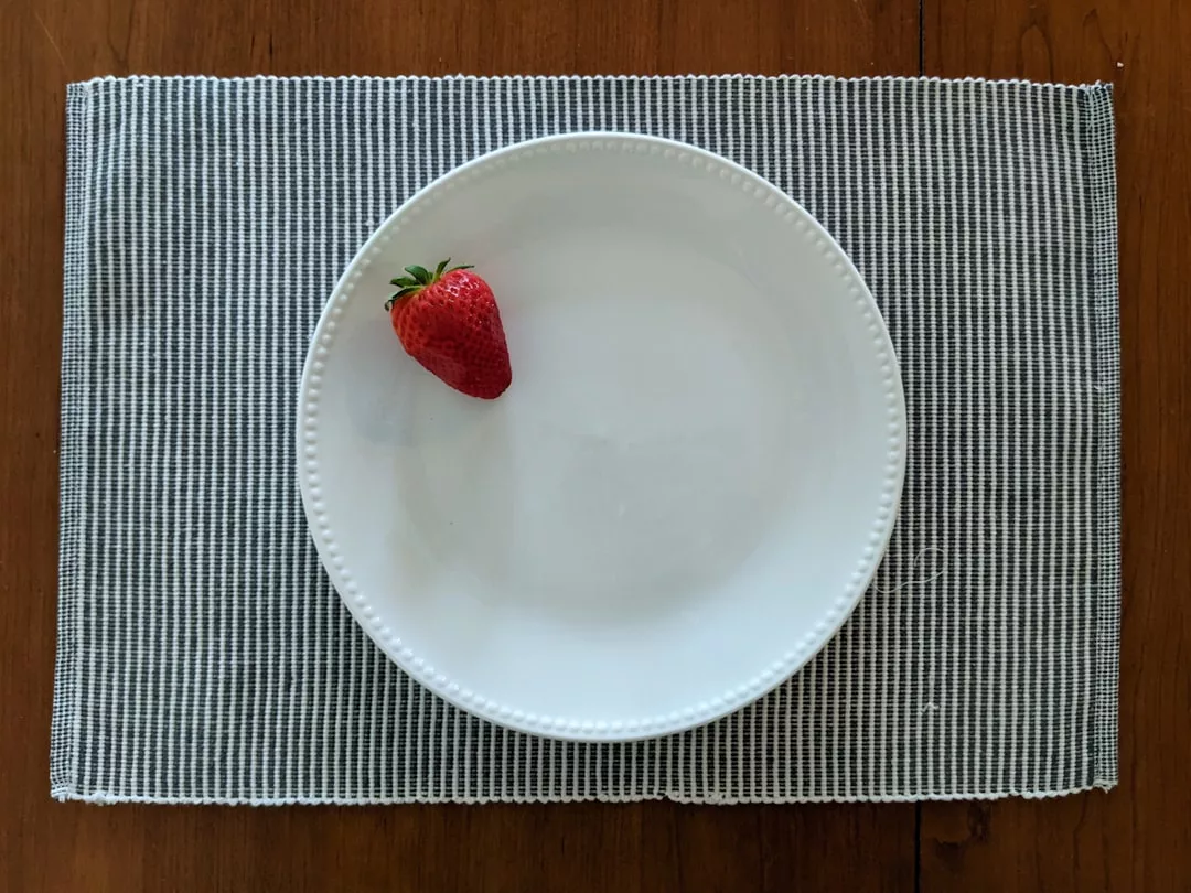 A single strawberry on a white plate, set on a woven gray placemat on a wooden table—a minimalist touch often seen in modern restaurants around Palma Nova known for their creative tapas fusion.