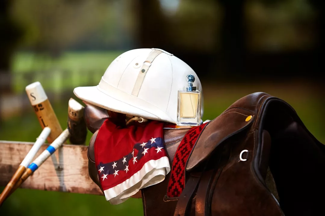 A white polo helmet, red patterned scarf, and perfume bottle rest on a leather saddle with polo mallets nearby—an arrangement that evokes exclusive equestrian experiences like VIP riding lessons at fincas near Llucmajor.
